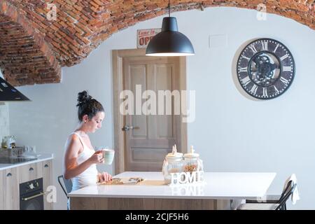 young brunette girl reading a magazine while drinking coffee in the kitchen