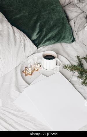 Christmas festive still life. Blank papers invitation mockups with cup of coffee, gingerbread cookie and spruce tree branches on ceramic plate Stock Photo