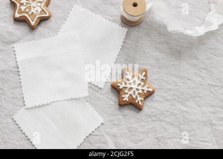 Christmas fabric samples mockup scene. White cotton textile squares on linen table cloth background. Gingerbread cookies, decorative sugar frosting Stock Photo