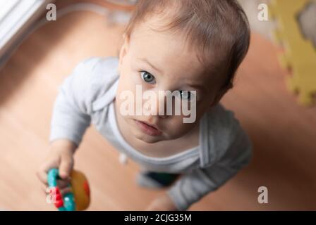 Little boy looks surprised up into the camera. Shooting from above. Child 1 year old boy indoor. Stock Photo