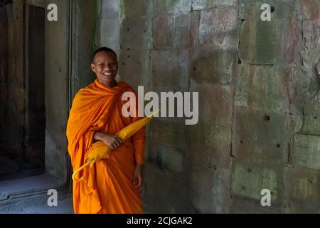 Portrait of happy young monk in orange robe holding the orange umbella in the Angkor Wat ancient temple Stock Photo