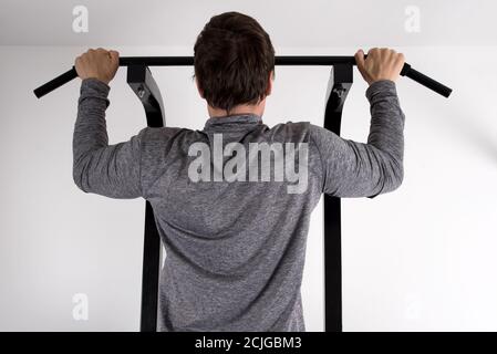 Closeup back view of a young fit male doing a pull-up on a machine at the gym Stock Photo