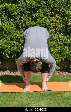 Vertical shot of a young fit male doing the forward fold yoga pose outdoors Stock Photo