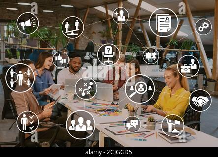 Business employment. Team of young designers working on new project together sitting in office. Collage with icons Stock Photo