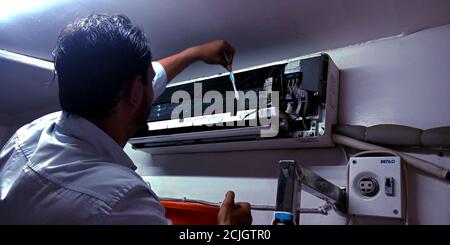 DISTRICT KATNI, INDIA - AUGUST 04, 2019: An indian electric maintenance worker cleaning air conditioner on the wall. Stock Photo
