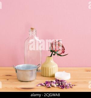Aroma therapy objects. Glass bottle, dry rose flower, candle on wooden table with pink background Stock Photo