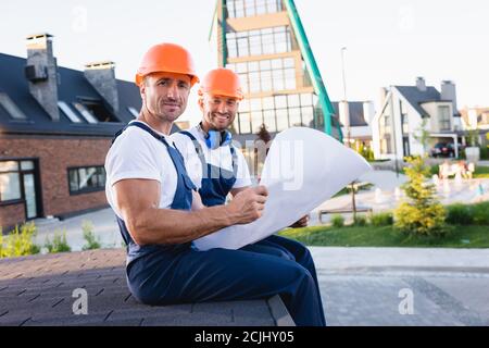 Workmen in overalls holding blueprint on roof of building on urban street Stock Photo