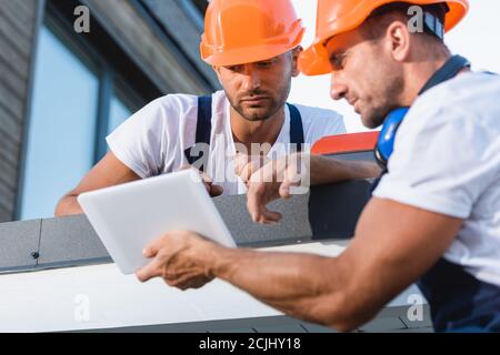 Selective focus of manual workers looking at digital tablet on roof of house Stock Photo