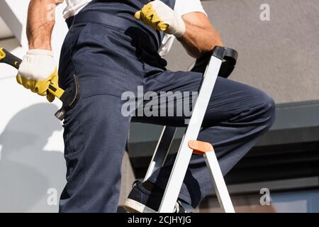 Cropped view of builder holding hammer while standing on ladder outdoors Stock Photo