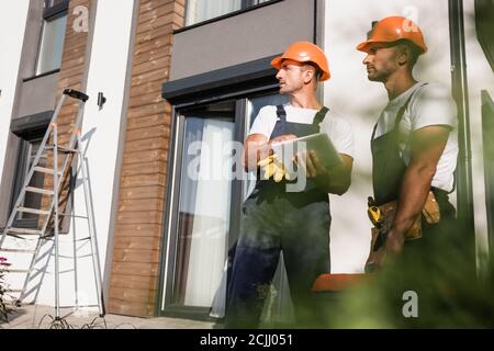 Selective focus of manual workers with toolbox using digital tablet near house outdoors Stock Photo