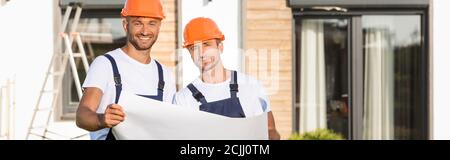 Horizontal crop of builders in hardhats holding blueprint outdoors Stock Photo