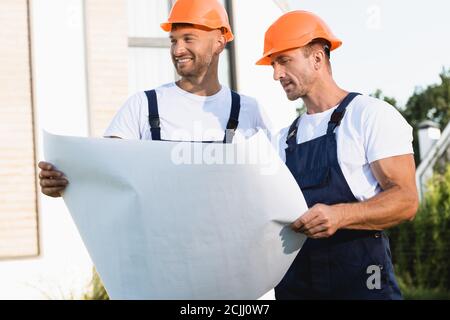 Builders in hardhats and uniform holding blueprint outdoors Stock Photo