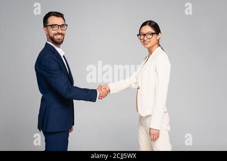 couple of interracial business partners shaking hands while looking at camera isolated on grey Stock Photo