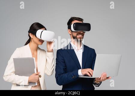 businesswoman touching vr headset near businessman using laptop isolated on grey Stock Photo