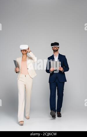 full length view of business partners in vr headsets holding folders while walking on grey Stock Photo