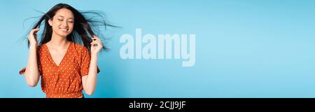 horizontal concept of stylish asian woman in red blouse posing on wind on blue Stock Photo