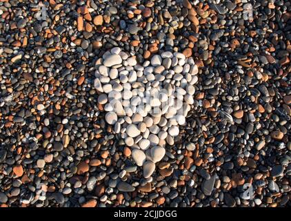 A heart drawn by light pebbles against a background of dark pebbles. World Heart Day. Sea shells. Stock Photo