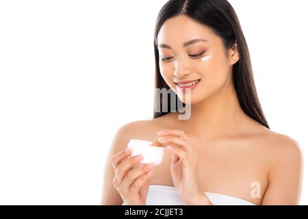 brunette asian woman touching cosmetic cream while applying it on face isolated on white Stock Photo