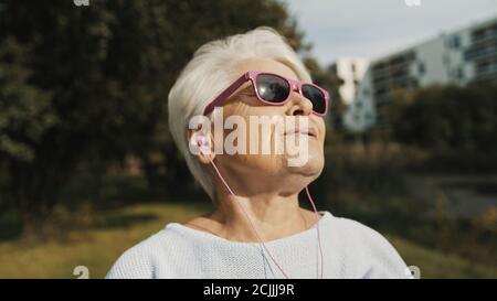 Senior woman with pink sunglasses in the park looking at the distance. High quality photo Stock Photo