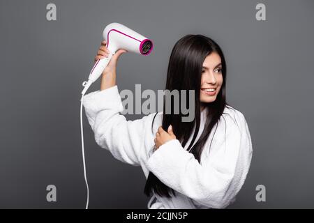 brunette long haired woman in bathrobe using hairdryer isolated on black Stock Photo