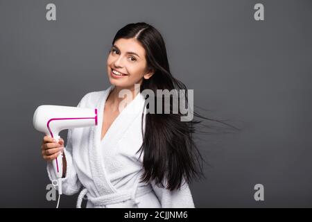 brunette long haired woman in bathrobe using hairdryer isolated on black Stock Photo