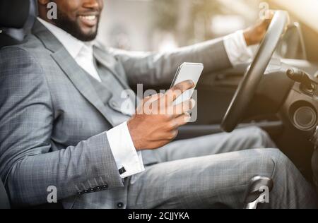 Black guy in suit using smartphone while driving Stock Photo