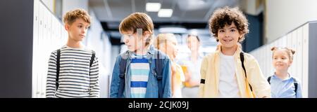 horizontal image of multicultural classmates walking along school corridor with teacher on background Stock Photo