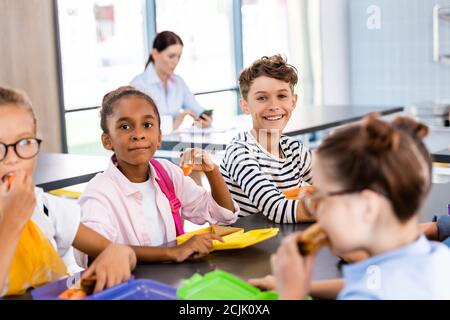 selective focus of multicultural schoolchildren having dinner in school eatery Stock Photo