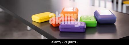 horizontal image of colorful plastic lunch boxes on table in school dining room Stock Photo