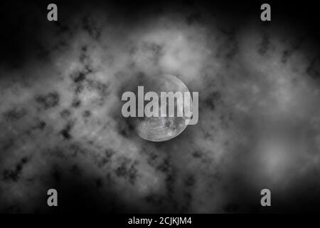 Grayscale shot of the full moon hiding behind dark clouds Stock Photo