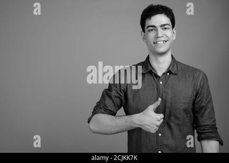 Portrait of happy young handsome Persian businessman giving thumbs up Stock Photo