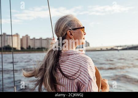 Side view of mature woman wearing sunglasses and looking to the distance while standing on the yacht Stock Photo