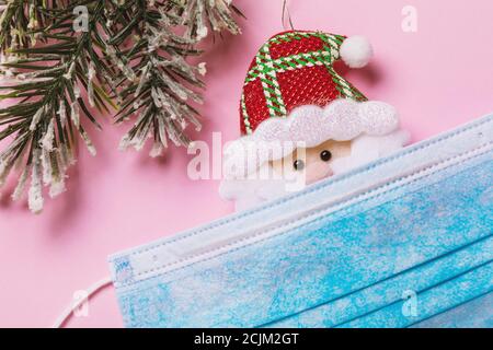Medical mask and toy Santa Claus on a pink background. Concept on the theme of quarantine for the Christmas holidays Stock Photo
