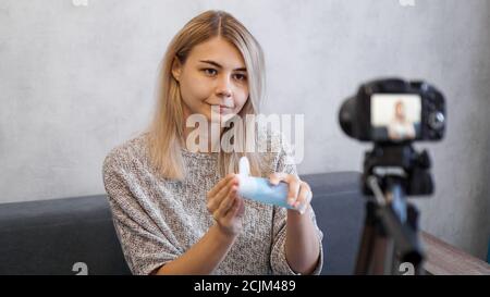 Cheerful female beauty blogger recording video at home. She shows lotion for skin. Stock Photo