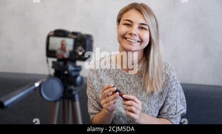 Vlogger female showing lipstick. Beauty blogger woman filming daily make-up routine tutorial near camera on tripod Stock Photo