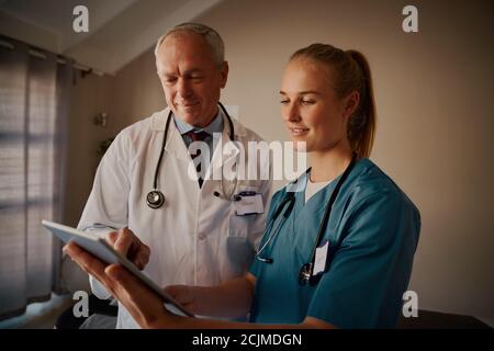 Young female nurse in conversation with senior male doctor discussing medical reports on digital tablet in hospital Stock Photo