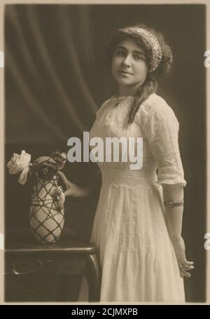 Antique c1920 photograph, portrait of a woman, age about 20-24, with a vase of flowers. Exact location unknown, probably New England, USA. SOURCE: ORIGINAL PHOTOGRAPH Stock Photo