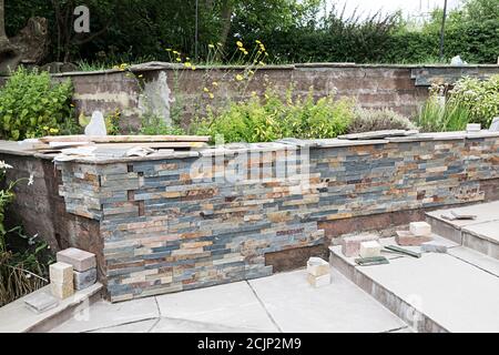 Stone cladding being installed on garden retaining wall, UK Stock Photo