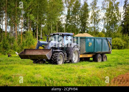 Silver Valtra farm tractor with Multiva trailer load of harvested grain by field on a clear day of autumn harvest. Koski Tl, Finland. September 11, 20 Stock Photo