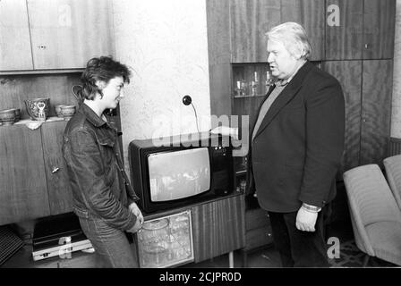 30 November 1986, Saxony, Sitzenroda: A colour television set from RFT in a GDR wall unit is explained to a teenager in the mid-1980s by an adult man. Exact date of recording not known. Photo: Volkmar Heinz/dpa-Zentralbild/ZB Stock Photo