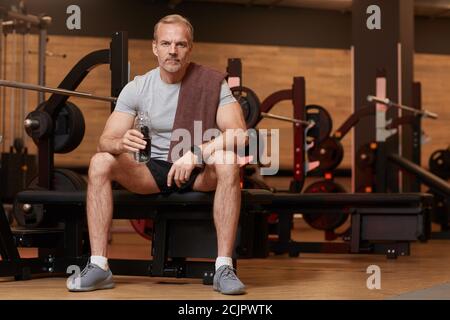 Portrait of mature man drinking water and looking at camera while sitting and resting after sports training Stock Photo