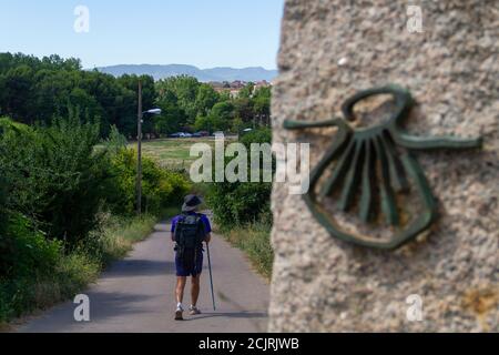Pilgrim on the route of the Camino de Santiago (Way of Saint James) passing next to the scallop shell that marks the way Stock Photo