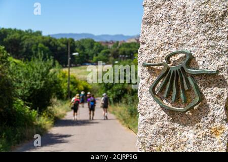 Pilgrims on the route of the Camino de Santiago (Way of Saint James) passing next to the scallop shell that marks the way Stock Photo