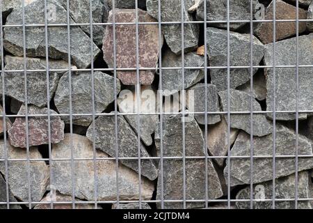 Stacked cobblestones, fixed with steel mesh. Wall of stones under metal grid. Stock Photo