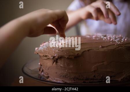 Close Up of a Child's Hand Decorating a Chocolate Frosted Birthday Cake with Sprinkles Stock Photo