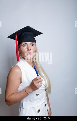 Beautiful blonde graduation cap holds a laptop in her hand, studio light background. Concept, education, learning remotely, online. High quality photo Stock Photo