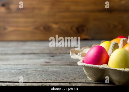 Dyed easter eggs in cardboard box on wooden background. Stock Photo
