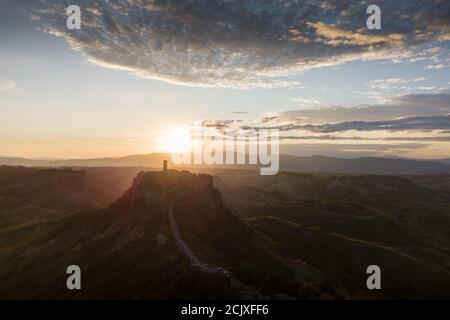 Aerial view of stone town Civita di Bagnoregio with the sun at the sunrise with clay badlands and trees in background