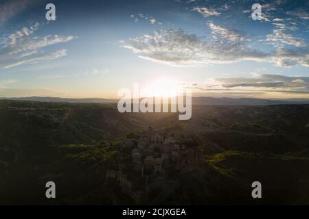 Aerial view of stone town Civita di Bagnoregio with the sun at the sunrise with clay badlands and trees in background