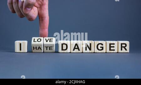 Hand turns cubes and changes the expression 'I hate danger' to 'I love danger'. Beautiful grey background, copy space. Concept. Stock Photo